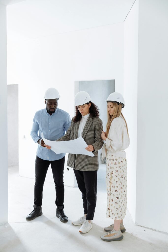 Testimonials Three people in hard hats examining construction plans in a new home